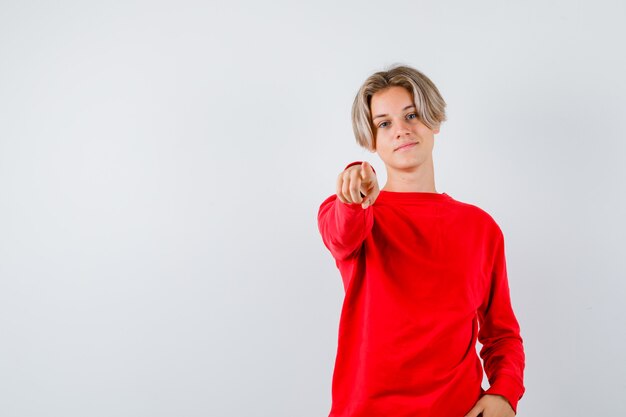 Teen Boy im roten Pullover zeigt nach vorne und sieht selbstbewusst aus, Vorderansicht.