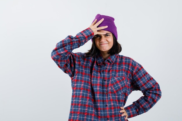 Teen Frau in kariertem Hemd lila hält eine Hand auf dem Kopf, eine andere Hand auf der Hüfte
