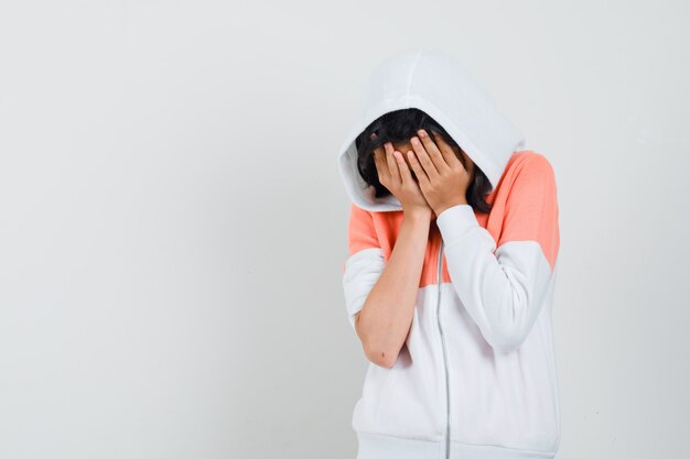 Teen Girl in Jacke, die Gesicht mit ihren Händen bedeckt und traurig aussieht.