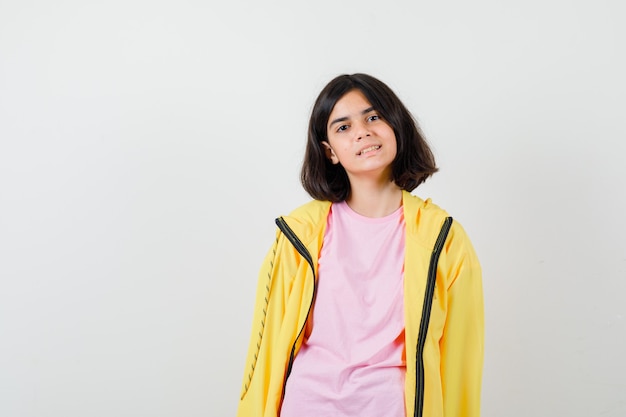 Teen Girl posiert beim Stehen in T-Shirt, gelber Jacke und selig aussehend. Vorderansicht.