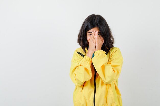 Teen Mädchen in gelber Jacke Händchen haltend im Gesicht und ängstlich aussehend, Vorderansicht.