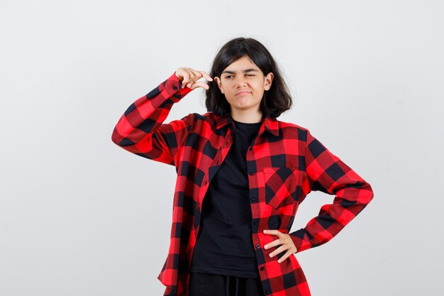 Teen Mädchen mit kleinem Schild in T-Shirt, kariertem Hemd und cool aussehend, Vorderansicht.