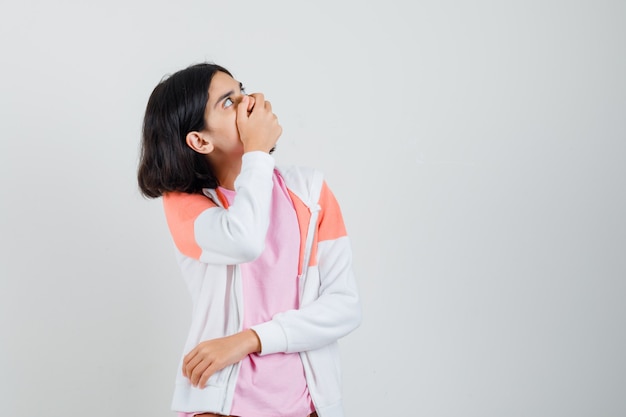 Teen Mädchen schaut auf, während Hand auf ihrem Mund in Jacke, rosa Hemd hält und erstaunt schaut.