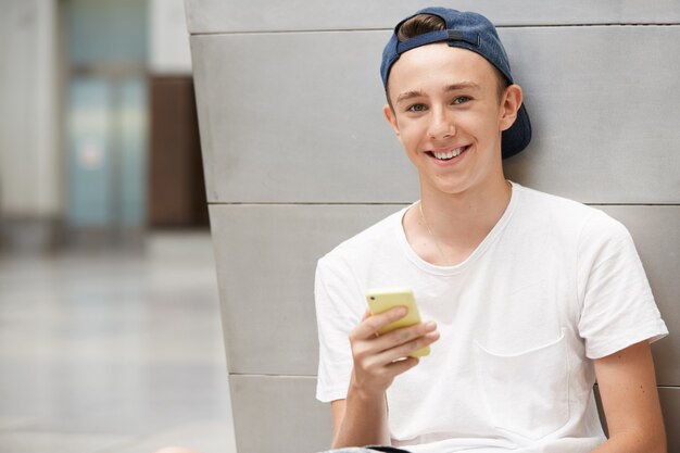 Teenager, der Kappe trägt und Smartphone verwendet