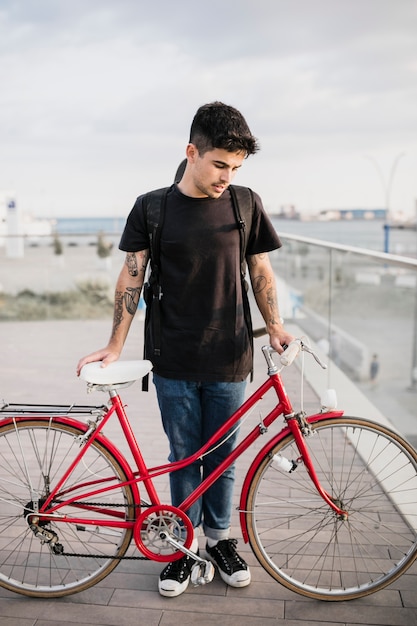 Teenager, der mit rotem Fahrrad auf Promenade steht