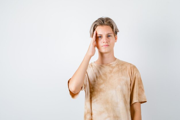 Teenager-Junge, der Hand an den Tempeln im T-Shirt hält und traurig aussieht. Vorderansicht.