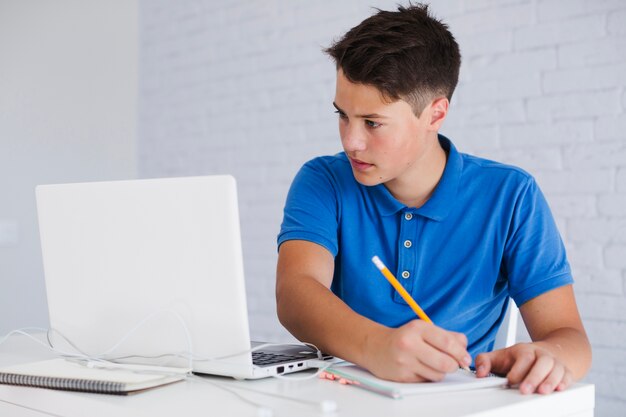 Teenager macht Notizen Blick auf Laptop