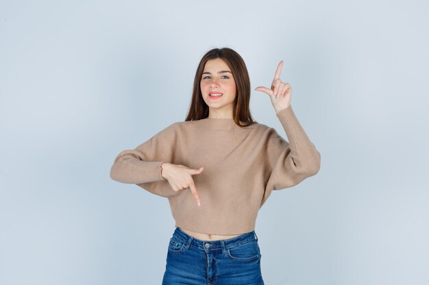Teenager-Mädchen, das in Pullover, Jeans und fröhlichem Aussehen in die entgegengesetzten Richtungen zeigt. Vorderansicht.