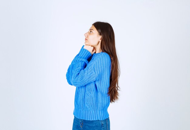 Teenager-Mädchen im blauen Pullover, der an etwas auf Weiß denkt.