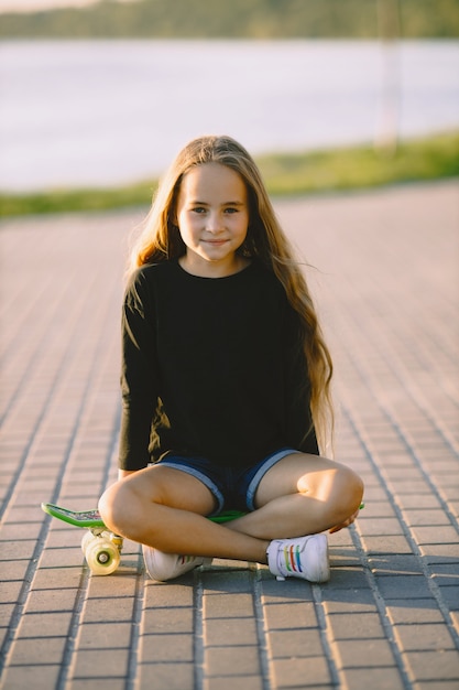 Teenager-Mädchen mit Skateboard am See sitzen