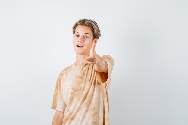 Teenagerjunge, der mit der Fingerpistole im T-Shirt nach vorne zeigt und selbstbewusst aussieht. Vorderansicht.