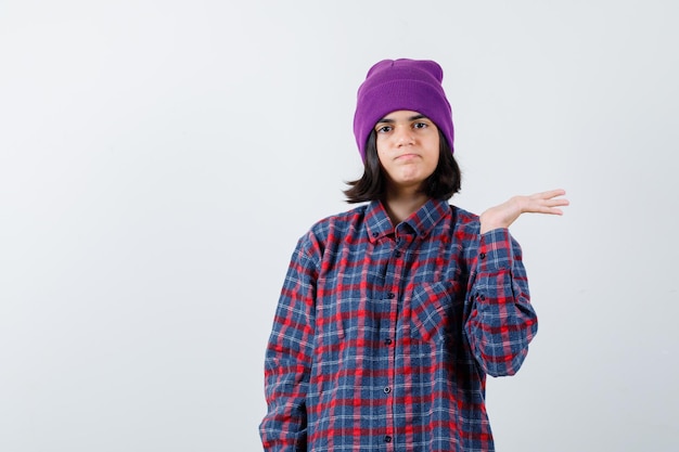 Teenie-Frau, die etwas in kariertem Hemd und Mütze hält und vorsichtig aussieht