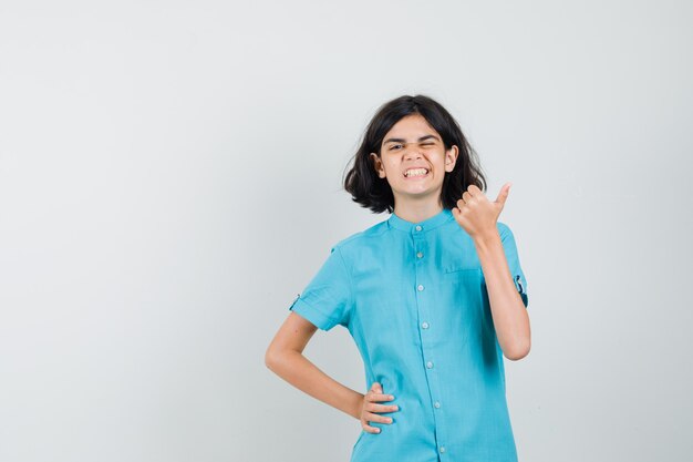 Teenie-Mädchen im blauen Hemd, das Daumen oben zeigt, während sie zwinkert und optimistisch aussieht