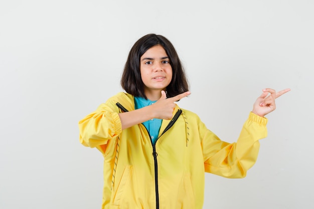 Teenie-Mädchen in gelber Jacke, die nach rechts zeigt und fröhlich aussieht, Vorderansicht.