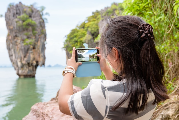 Teens girl tourist shooting foto wahrzeichen eine wunderschöne landschaft mit malerischer aussicht per handy auf koh tapu oder james bond island im ao phang nga bay national park, woman travel natur asien in thailand