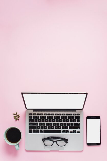 Teetasse; Brille; Handy und ein offener Laptop mit weißem Bildschirm vor rosa Hintergrund