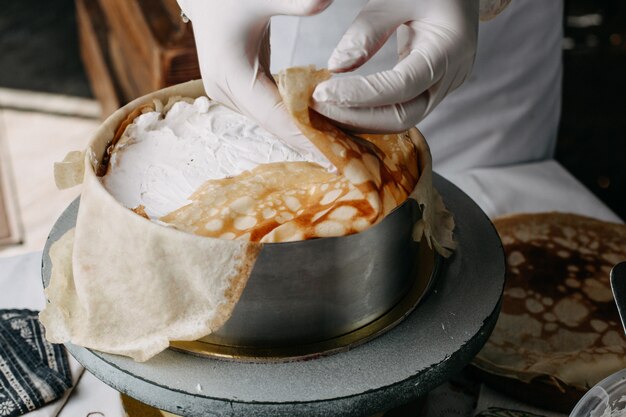 Teig in der runden Pfanne mit Koch, der saure Sahne darauf innerhalb der Küche verteilt