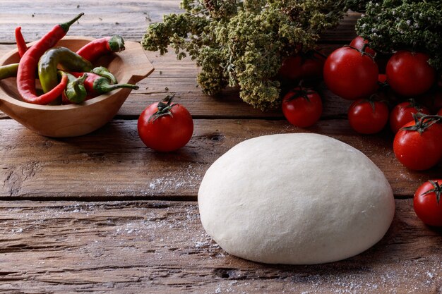 Teigklumpen auf einem Holztisch, umgeben von Tomaten und Pfeffer