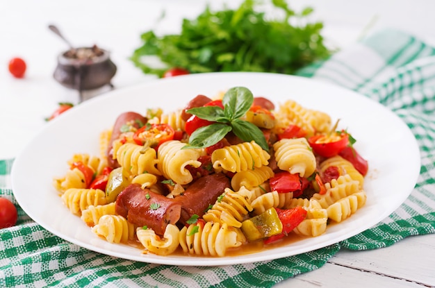 Teigwaren mit Tomatensauce mit Wurst, Tomaten, grüner Basilikum verziert in der weißen Platte auf einem Holztisch.