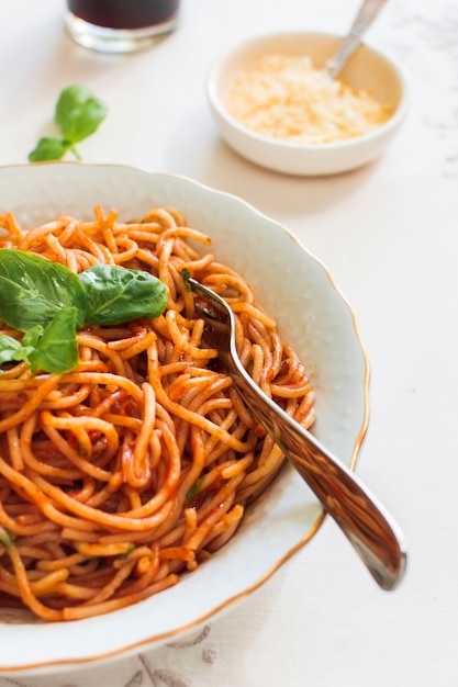 Teigwaren mit Tomatensauce und Basilikum auf keramischer Platte mit Gabel