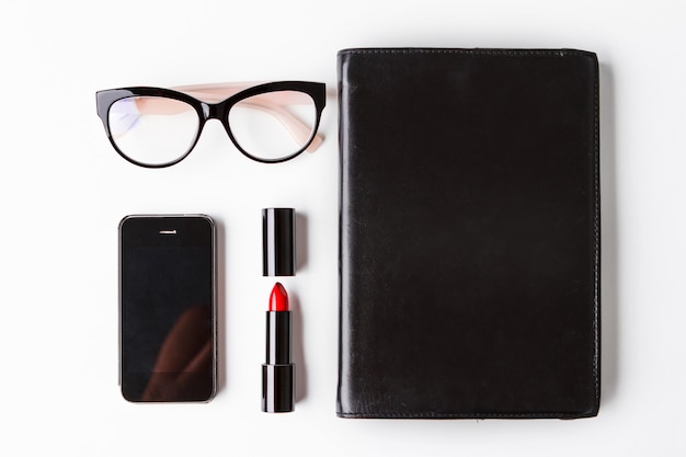 Telefon und Notizbuch der roten Lippenstiftbrille über weißem Hintergrund