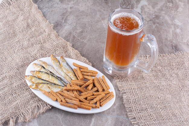 Teller mit Fisch und Crackern mit Bier auf Marmoroberfläche. Foto in hoher Qualität
