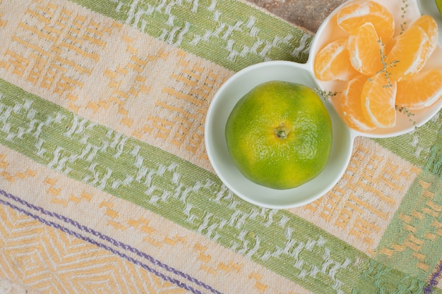 Teller mit frischen mandarinen und segmenten auf tischdecke.