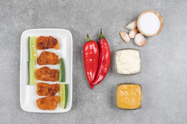 Teller mit gebratenen Nuggets und frischem Gemüse auf Marmoroberfläche