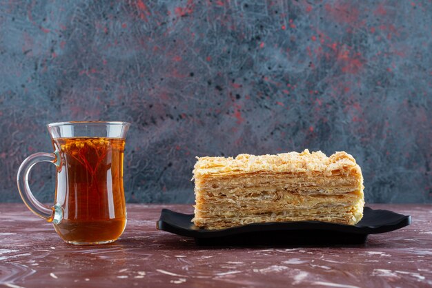 Teller mit geschnittenem Kuchen und Glas Tee auf burgunderfarbener Oberfläche.