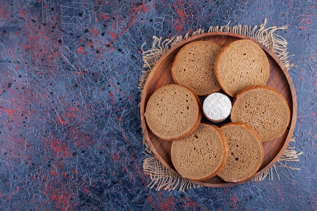 Teller mit geschnittenem schwarzem Roggenbrot und Sahne auf blauer Oberfläche.