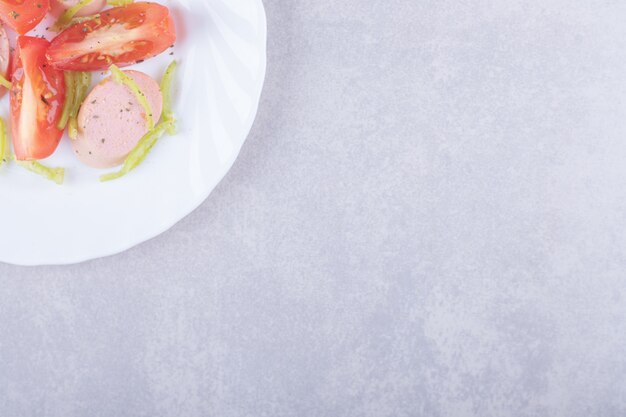 Teller mit geschnittenen Würstchen und Tomaten auf Steinhintergrund.