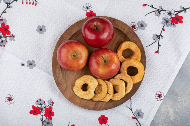 Teller mit getrockneten Apfelringen und frischen roten Äpfeln auf weißer Tischdecke.