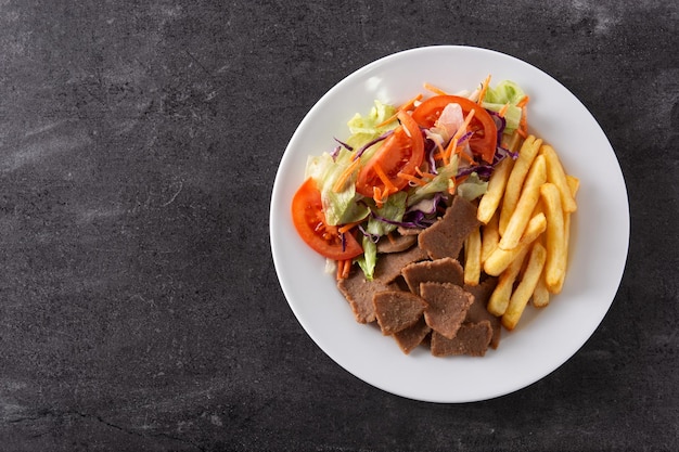 Teller mit Kebab, Gemüse und Pommes Frites auf schwarzem Steinhintergrund