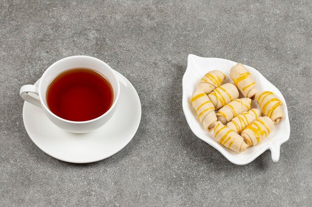 Teller mit Keksen und Tasse Tee auf Marmoroberfläche