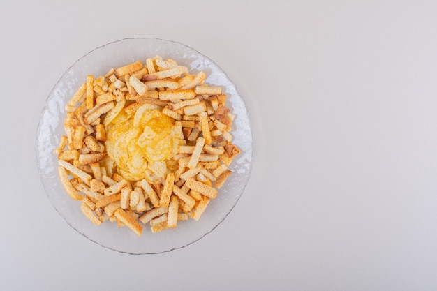 Teller mit leckeren knusprigen Crackern und Chips auf weißem Hintergrund. Foto in hoher Qualität