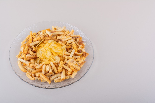 Teller mit leckeren knusprigen Crackern und Chips auf weißem Hintergrund. Foto in hoher Qualität