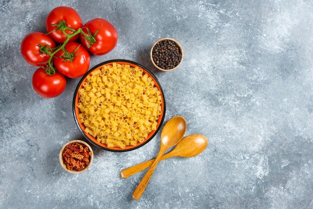 Teller mit Nudeln und Schüssel mit Tomaten auf Marmorhintergrund.