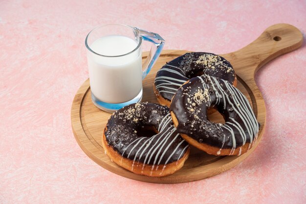 Teller mit Schokoladenkrapfen mit einem Glas Milch auf rosa Oberfläche.