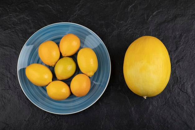 Teller mit Zitronen und reife Melone auf schwarzem Tisch.