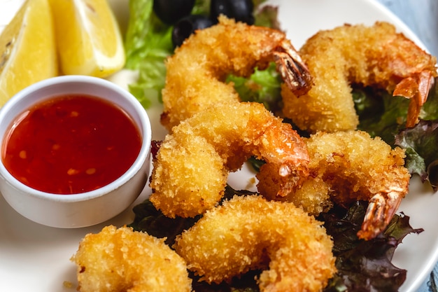 Tempura-Garnelen von der Seite mit süßer Chilisauce Zitronenscheibe und schwarzer Olive auf einem Teller