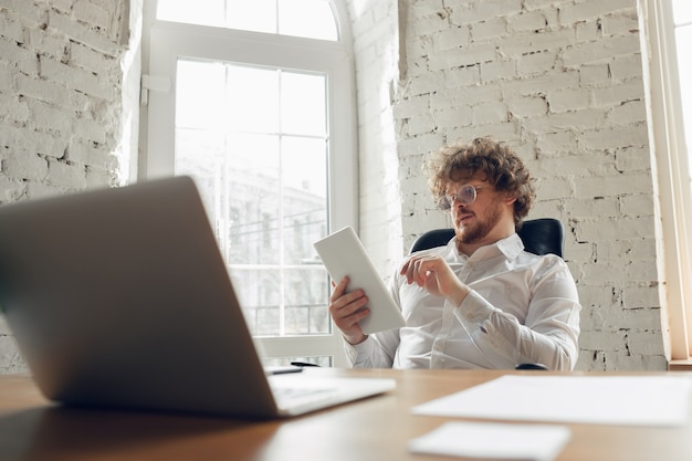 Text eingeben, analysieren, surfen. Kaukasischer junger Mann in Geschäftskleidung, der im Büro arbeitet. Junge Geschäftsfrau, Managerin, die Aufgaben mit Smartphone, Laptop, Tablet erledigt, hat Online-Konferenz und studiert.