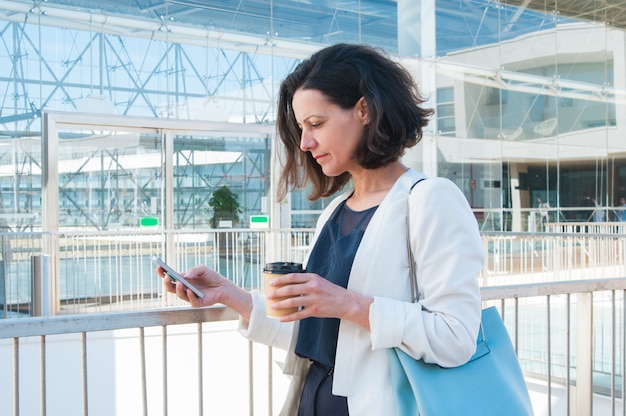 Texting Mitteilung der ernsten mittleren erwachsenen Geschäftsfrau an der Kaffeepause