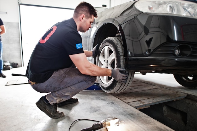 Kostenloses Foto thema autoreparatur und -wartung mechaniker in uniform, der im autoservice arbeitet und reifen überprüft