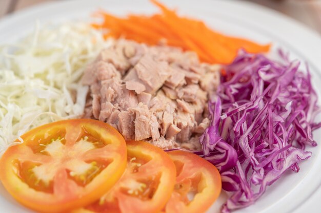 Thunfischsalat mit Karotten, Tomaten, Kohl auf einem weißen Teller auf einem Holzboden.