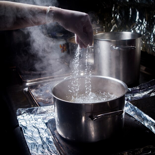 Tiefer Topf der Seitenansicht mit kochendem Wasser und Salz und menschlicher Hand im Ofen