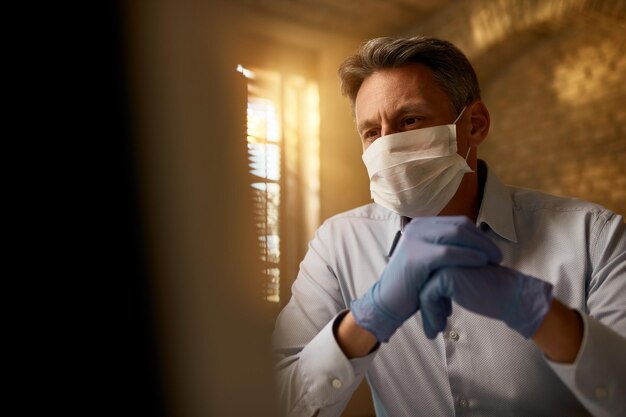 Tiefwinkelansicht des Unternehmers, der eine Gesichtsmaske trägt, während er den Computer benutzt und während der Coronavirus-Epidemie arbeitet