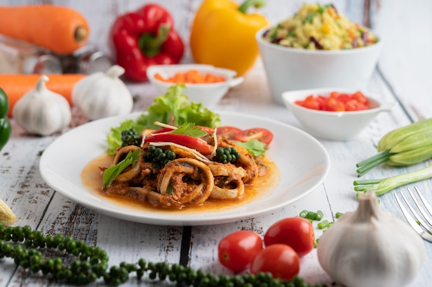 Tintenfisch gebraten mit Curry-Paste in weißen Teller, mit Gemüse und Beilagen auf einem weißen Holzboden.