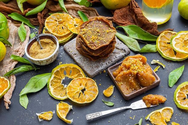 Tisch mit trockenen Zitrusfrüchten und rohen Pfannkuchen in der Nähe einer Schüssel voller Mandarinenmarmelade