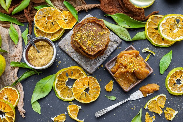 Tisch mit trockenen Zitrusfrüchten und rohen Pfannkuchen in der Nähe einer Schüssel voller Mandarinenmarmelade