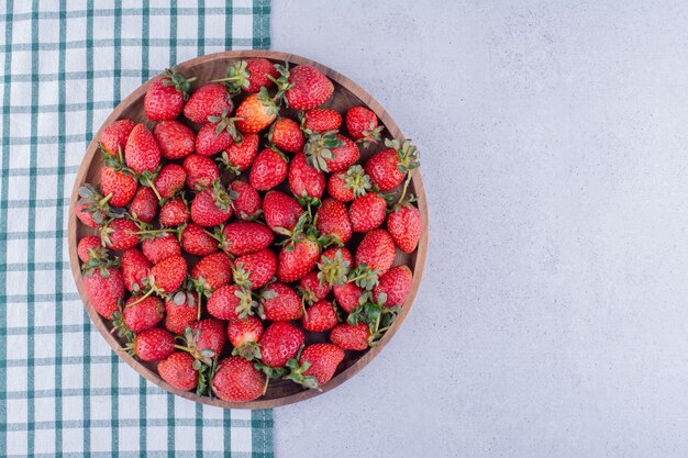 Tischdecke unter einer großen Schüssel voller Erdbeeren auf Marmorhintergrund. Foto in hoher Qualität